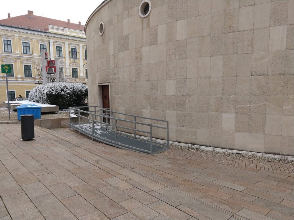 A fém rámpát fotóztuk, enyhe lejtésű, korláttal ellátott mindkét oldalán, előtte egy részen két lépcsőfok található, amely azonban sima tereppel folytatódik lépcső nélkül.
