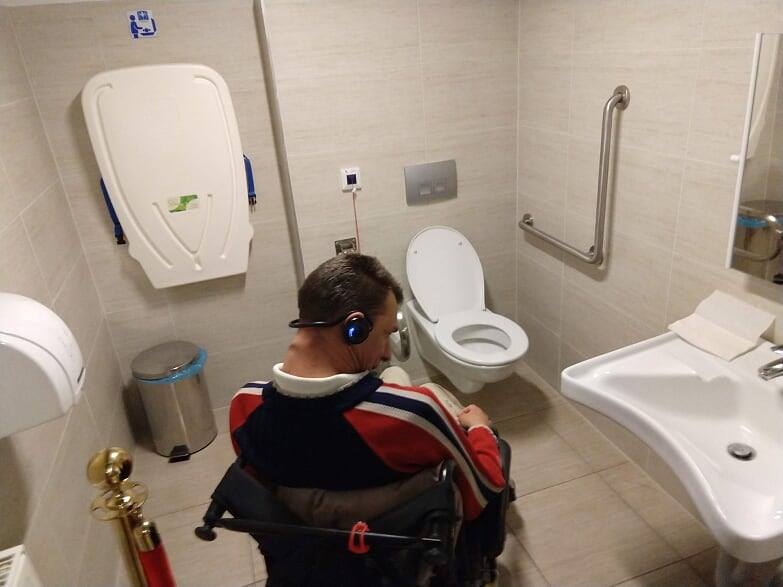 alakú, fém kapaszkodó.A WC felett gomb az öblítéshez, mellette lehajtható kapaszkodó, baloldalt a falon vészjelző berendezés. A kép jobboldalán mosdókagyló, állítható tükörrel. Szemben a fal jobboldalán lehajtható pelenkázóasztal, alul szemetesvödörrel.