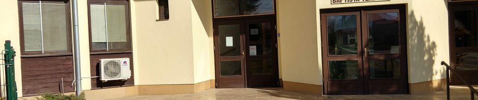 Kültéri kép, egy világossárga épület bejáratáról. Az ajtók, ablakok sötétbarnák. Az egyik ajtó felett Babtista Templom felirat található. A bejáratok előtt pár méterre két lépcsőfok van, a kép jobb oldalán pedig egy ezt megkerülő rámpa.