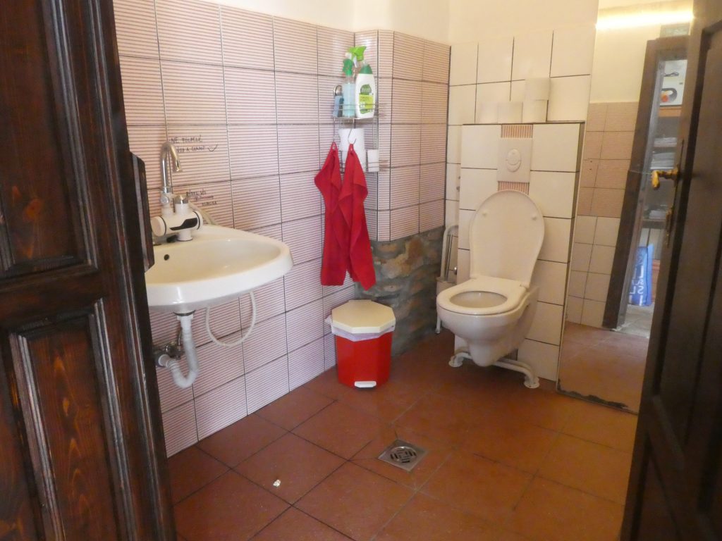 A WC tágas, belépve baloldalt a kézmosó, tovább balra a fal mellett a WC. Akadálymentes WC, ám a kapaszkodók a földön fekszenek, nincsenek felszerelve. Vészhívó nincsen.