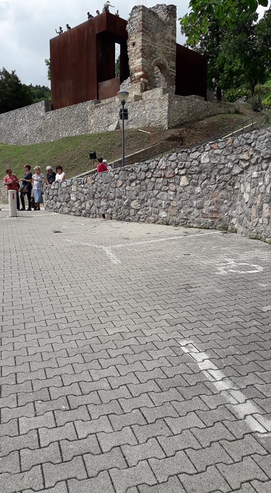 Tettyén a romoknál lévő kilátó alatt (amin épp hatan tartózkodnak a képen), két darab akadálymentes parkoló található egy kőfal mentén, amit a túrázók épp megközelítenek.