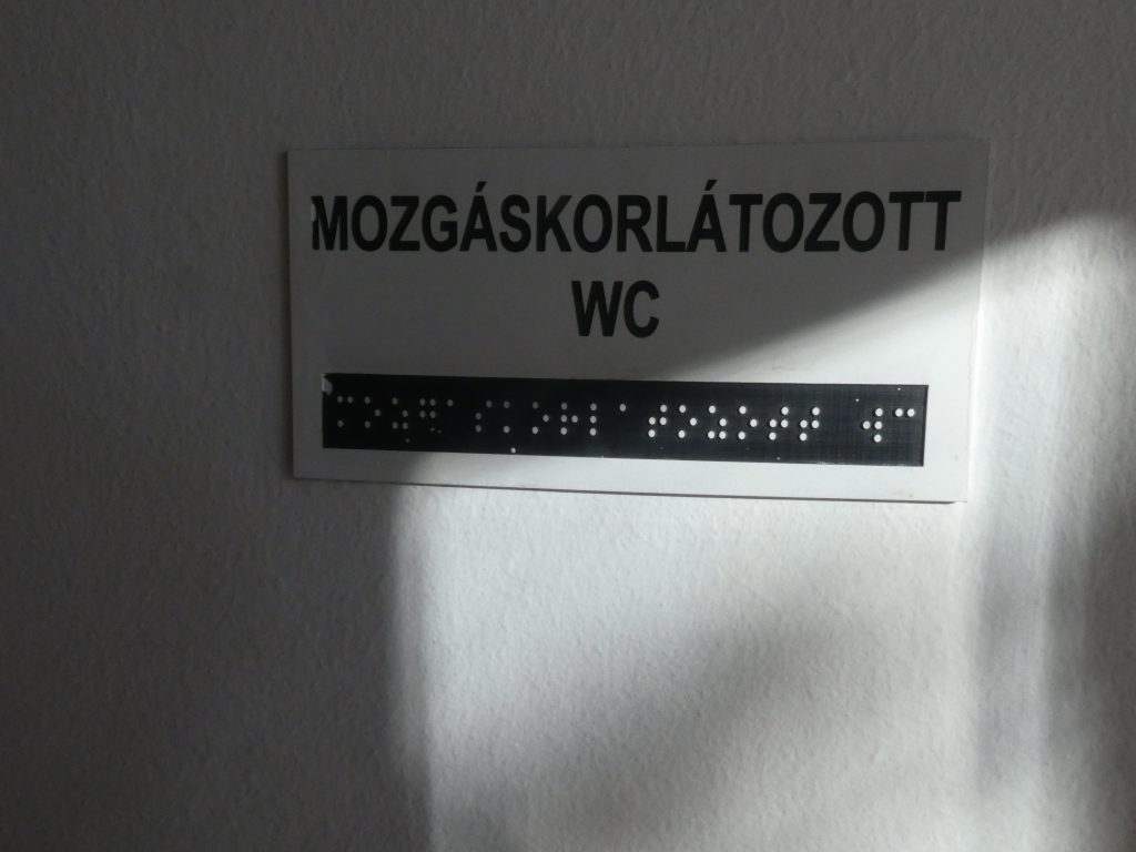 Szintén egy Braille felirattal ellátott tábla, Mozgáskorlátozott WC felirattal.