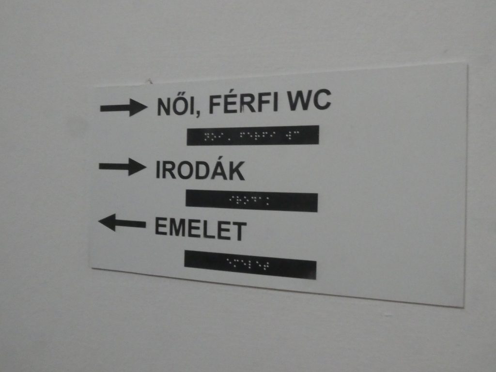 A feliratokat fotóztuk, melyek Braille felirattal ellátottak. Itt a Női, férfi WC-t, az irodákat és az emeletet jelzik éppen.