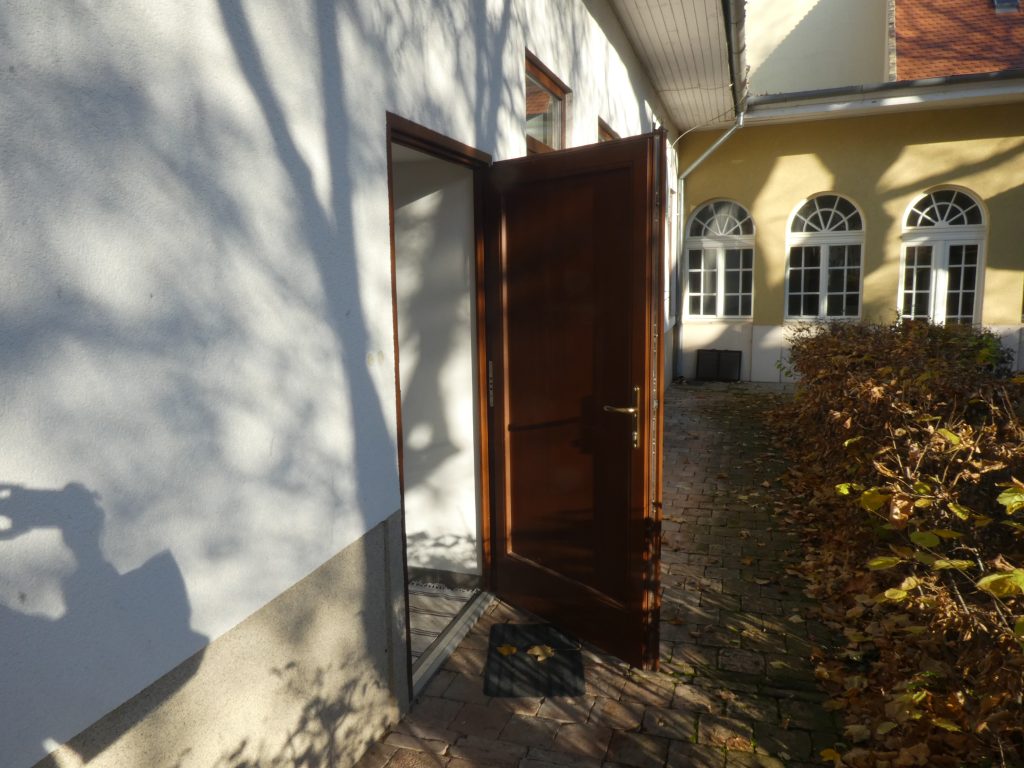 A kert felőli akadálymentes bejárat látszik, ajtaja nyitva. Nem önműködő ajtó, kifelé nyílik, a kerti járdáról megközelíthető.