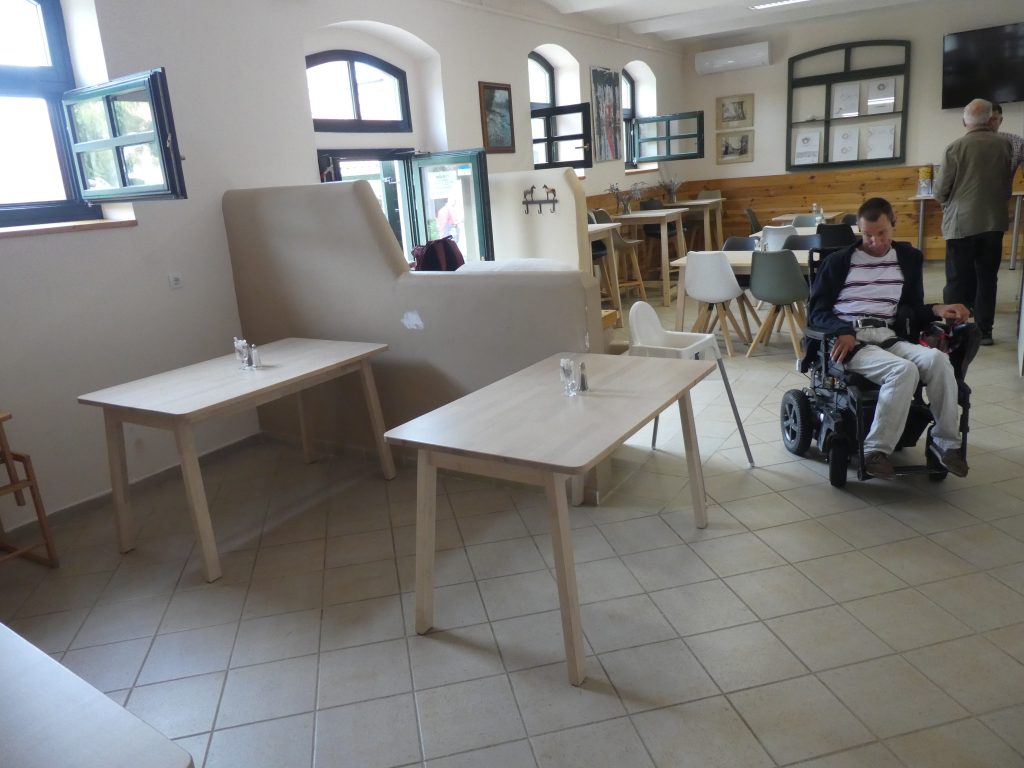 Az ebédlőrészt látjuk, fából készült négyszemélyes asztalok, székekkel. A burkolat világos padlócsempe.
