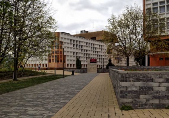 A Nevelési Központhoz vezető járdát látjuk, széles, sima betonlapokkal lerakott. kontrasztos színekkel ellátott.