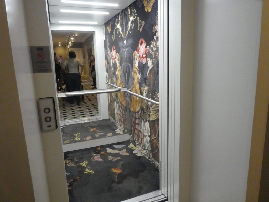 A padlószőnyeggel és szőnyegszerű burkolással ellátott lift belsejébe látunk be.