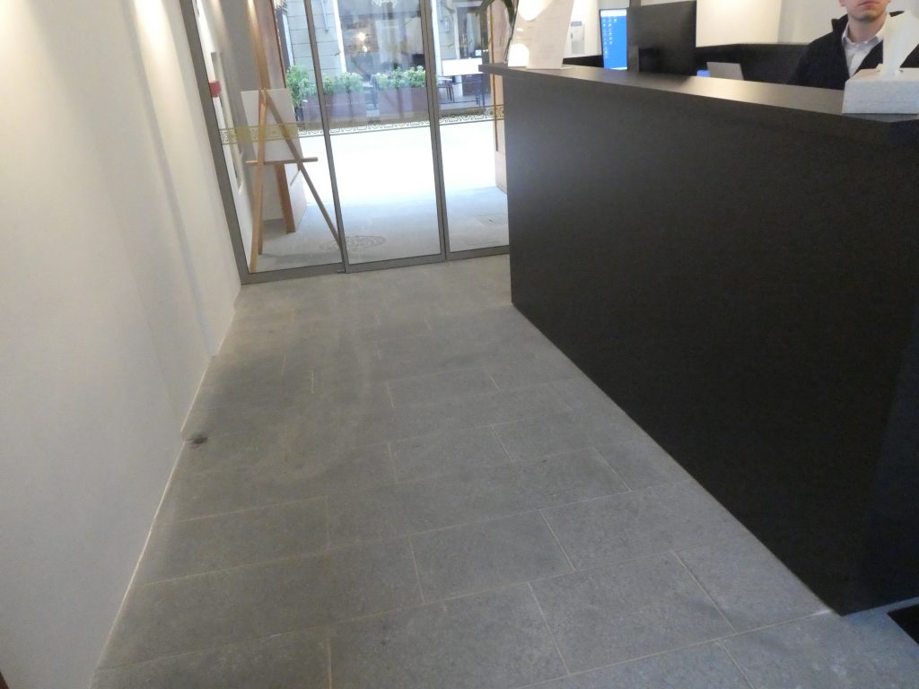 A recepció felől nézünk az utcai bejárat irányába. Látszik, hogy a recepcióhoz vezető kőborítású talaj emelkedik kicsit. A padló nem kontrasztos.