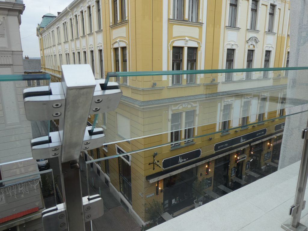A legfölső szinten lévő szobák teraszáról látunk le a Király utcára. A terasz korlátja üvegből van. Szemben a Városháza látszik.
