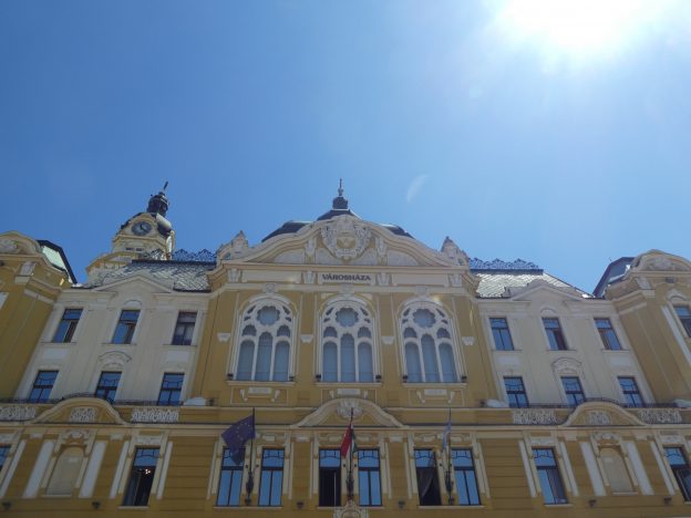 A városháza homlokzata, a fölső részre közelítve. Gyönyörű régi épület, itt középpontban a három hatalmas ablakot látjuk, háttérben kidugja a csúcsát a városháza tornya.