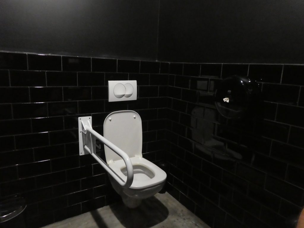 Belépve szemből a WC ülőke baloldalán lehajtható kapaszkodó. Jobb oldalán a fal felől semmilyen kapaszkodó sincs.