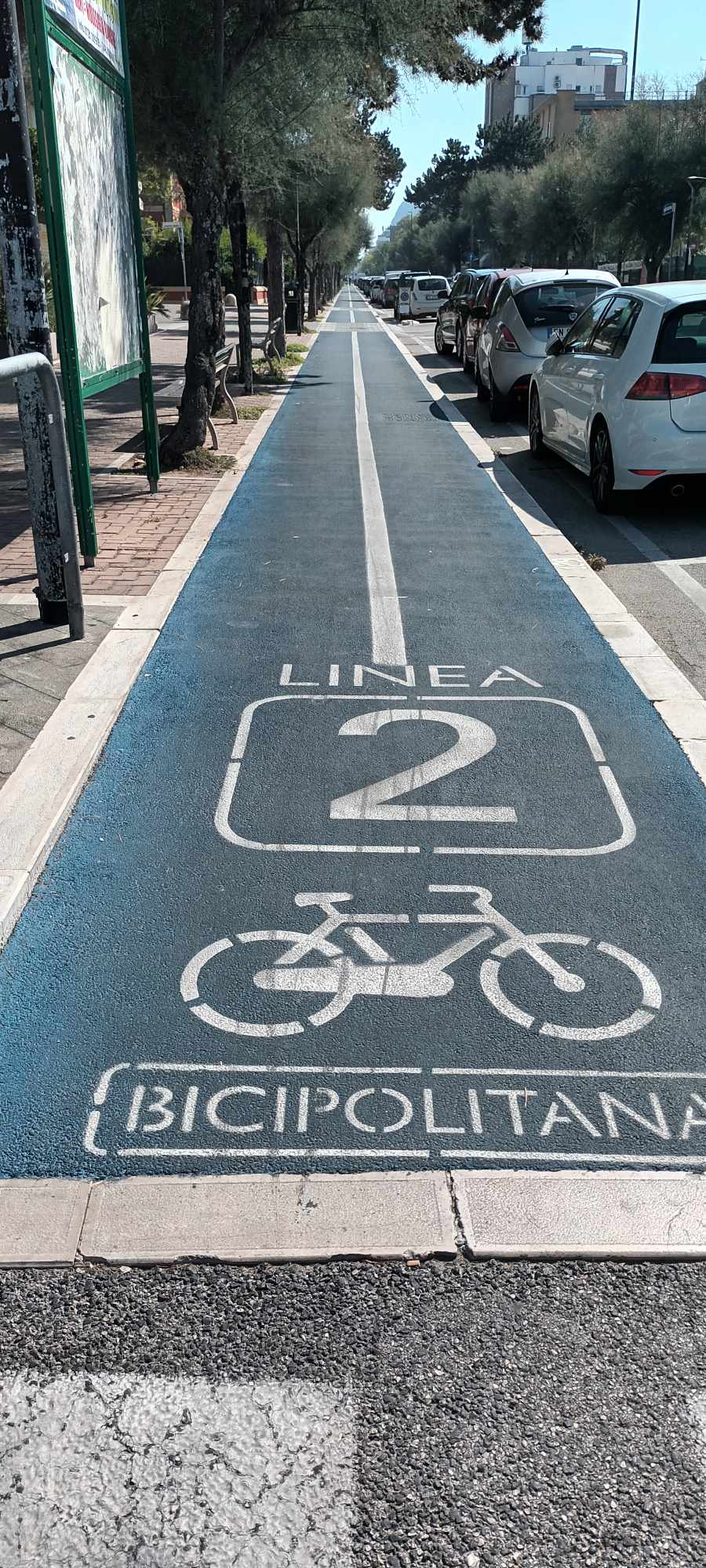 Sima, egyenes járdát látunk bicikliseknek, melyre a Linea 2 jel van festve, és egy biciklis ikon. 