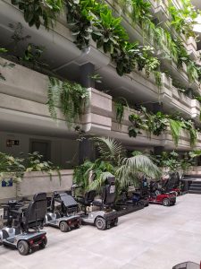 Egy szálloda földszintjét látjuk, ahol elektromos mopedek parkolnak. A szálloda belső folyosós és több emeletes. A folyosókról trópusi növények burjánzanak. 
