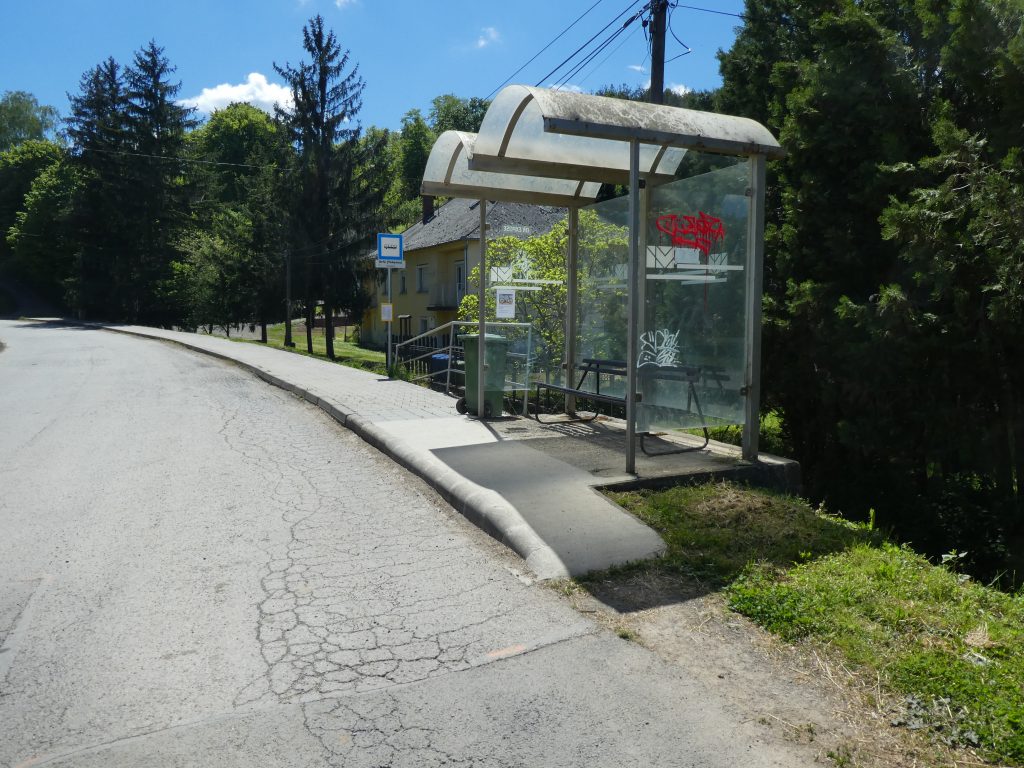 A tekeresi buszmegálló kicsit távolabbról. Modern, üvegből készült fedett buszmegálló, rámpával. A fedett részben egy nagyobb padon lehet várakozni. 
