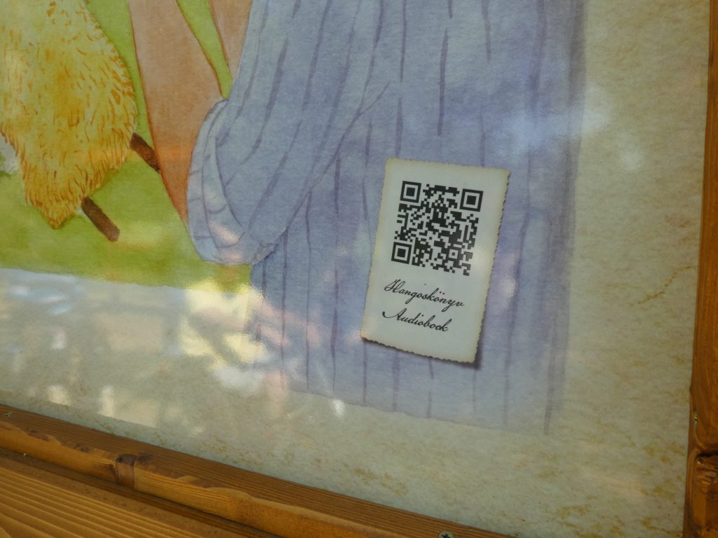 A mese táblák jobb alsó sarkában QR kódot látunk. A telefonnal ráközelítve elindul az adott meserészletet felolvasó hangoskönyv.