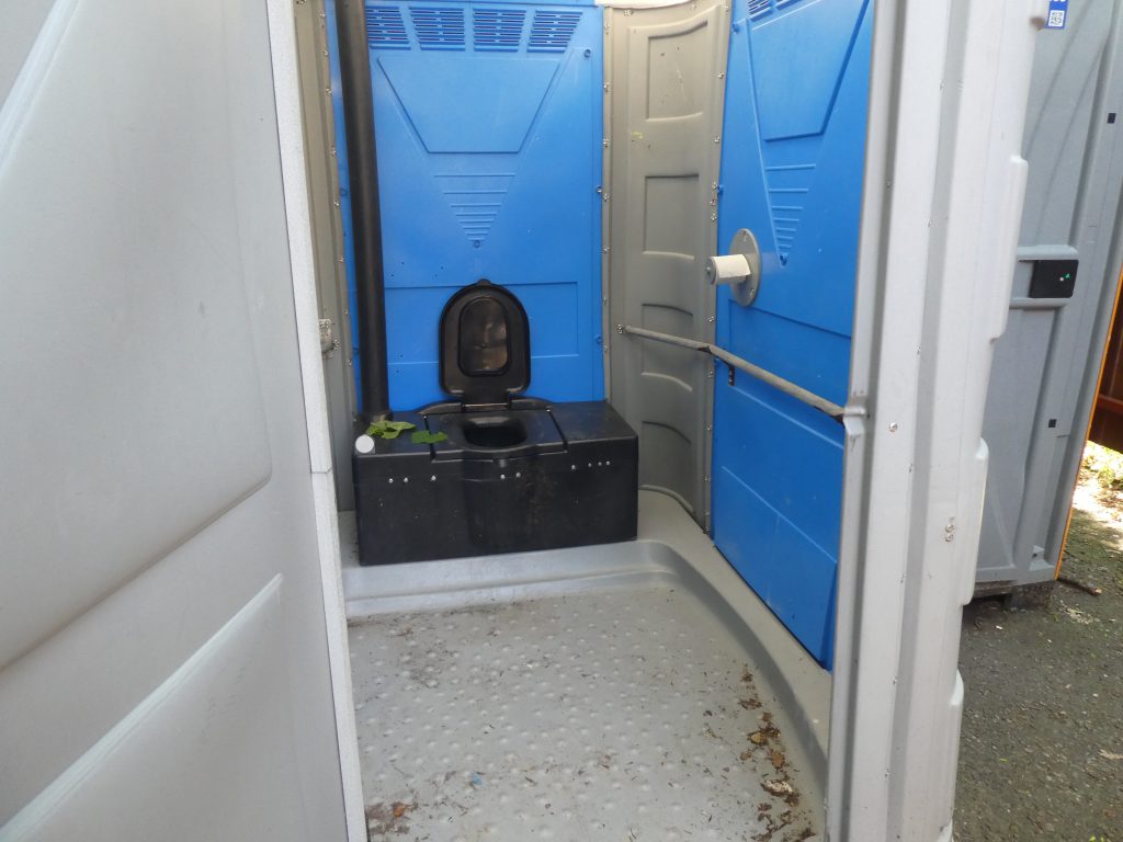 A mobil WC belsejét látjuk. Szélesebb jóval mint a szokásos toi toi WC-k. Belépve szemben található a WC ülőke, mely egy kisebb emelkedőn áll. Ezen a képen látható, hogy a WC-n ülve balról a falon található a WC-papír tartó, papírral.