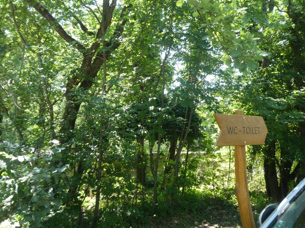 A WC-khez irányító fa tábla a parkolóban. Felirata: WC-Toilet