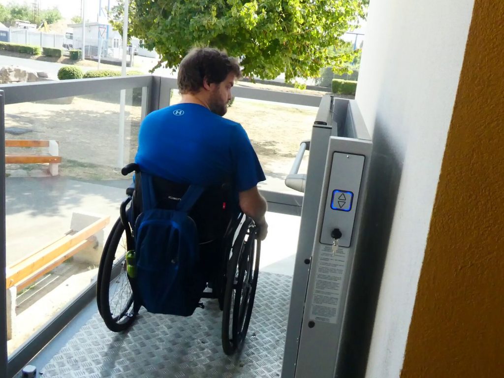 Gergő a külső liftben kerekesszékkel. Épp megérkezett a lépcsősor tetejére.