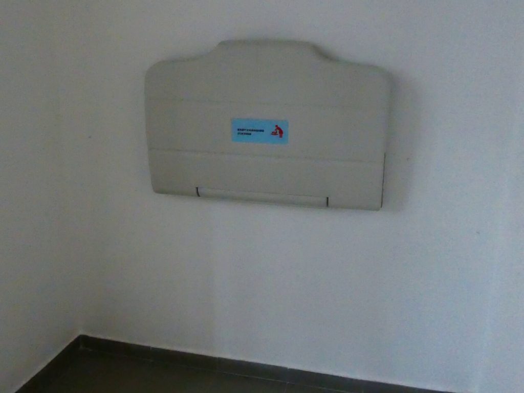 Az akadálymentes WC-ben a falra rögzítve egy felhajtható pelenkázóasztalt látunk. 
