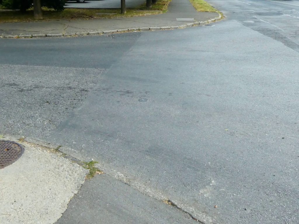 A Tüzér utca felől újabb járdarészletet látunk közelről. Itt sincsenek lekerekített járdák, hepehupás, régi betonjárdákat látunk. 