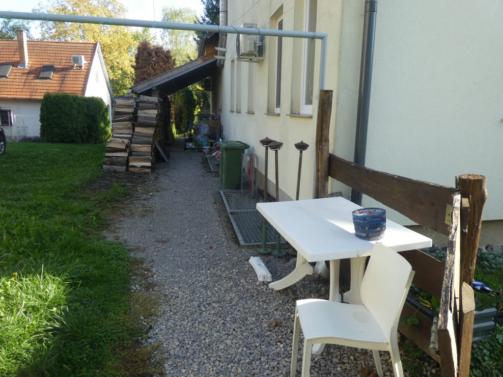 Az akadálymentes megközelítési lehetőség. Körben a felső parkolóból a terasz felé. Az első szakaszt fotóztuk, ami kiskaviccsal leszórt, az út mellett asztal, szék, néhány más használati eszköz.