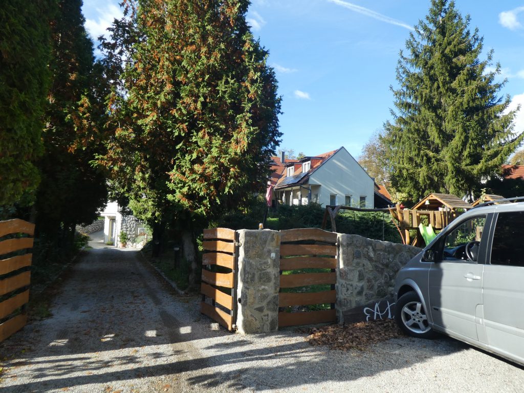 Bejárat az út felől. Fa kerítés, melynek dupla kapuján tudunk belépni a kertbe és elindulni a felfelé vezető autós úton. Itt parkoltunk mi is először az autóval.