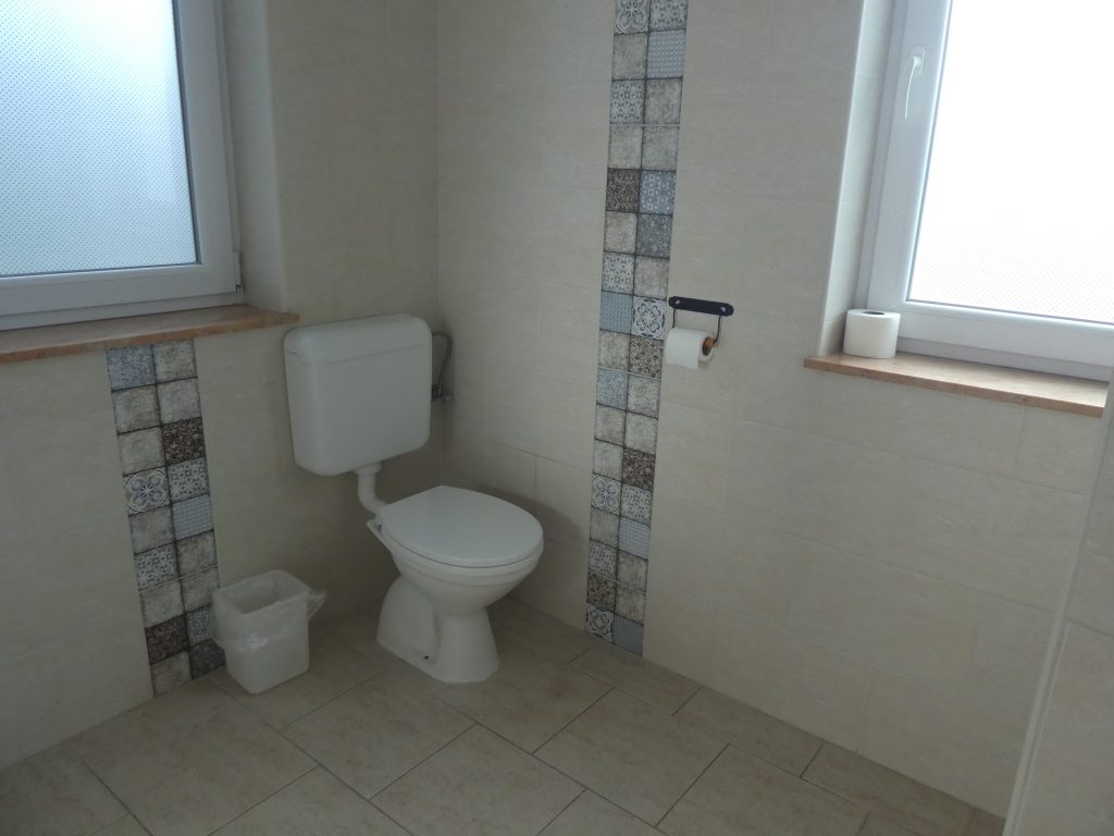 A fürdőszoba sarkában találjuk a WC-t. A fal mellé került a WC, jelenleg kapaszkodók nélkül.