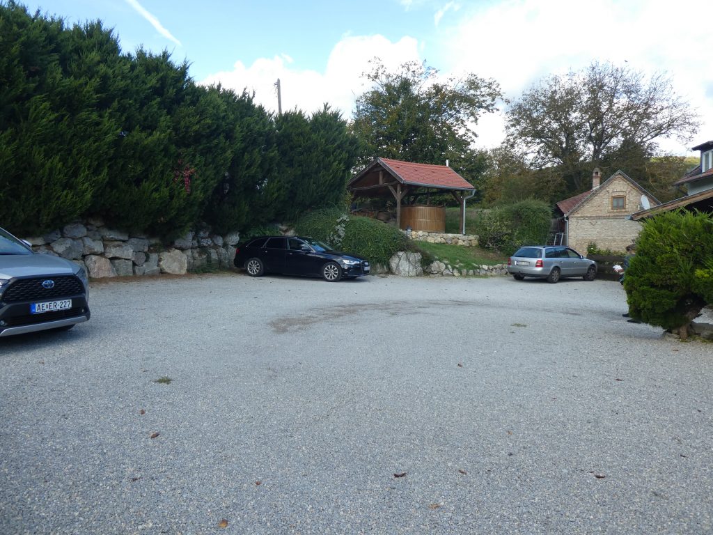 A fönti parkoló kiskavicsos burkolattal. A parkoló sarkában egy fedett helyen, hatalmas dézsát látunk, ebben is meg lehet merülni. A dézsa melletti területen lehet akadálymentesen megközelíteni az épületet.