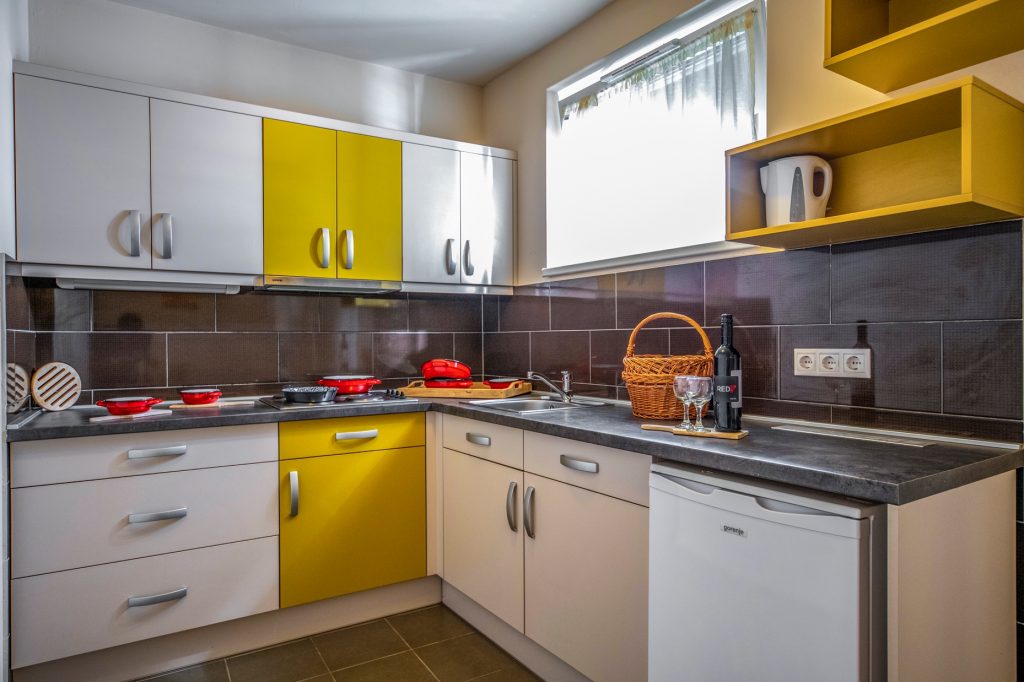 Az akadálymentes apartman konyhája, L alakban berendezve. A pult szélén hűtő található. A burkolat csempe.
