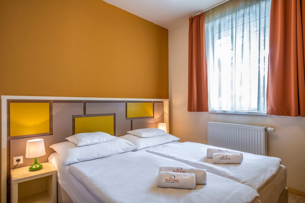 Az apartman hálószobájában két egymás mellé tolt ágy, az egyik oldalon éjjeli asztalkával. A képen nem látszik, hogy a fal felőli rész mennyire hozzáférhető kerekesszékkel.
