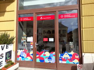 A Tourinform iroda bejárata a Széchenyi tér felől, az új külsővel. A három osztatú ajtó középső eleme nyílik befelé, nem automata. A bejárat előtt küszöb nincsen.