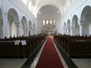 A teljes templombelső látható a főbejárattól. A főhajó egyenesen az oltárhoz vezet, kétoldalt régi faragott fa padok. Középen szőnyeg.